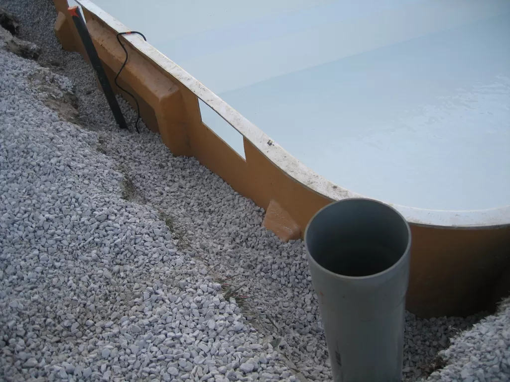 Remblai périphérique de la piscine coque avec du gravier concassé.